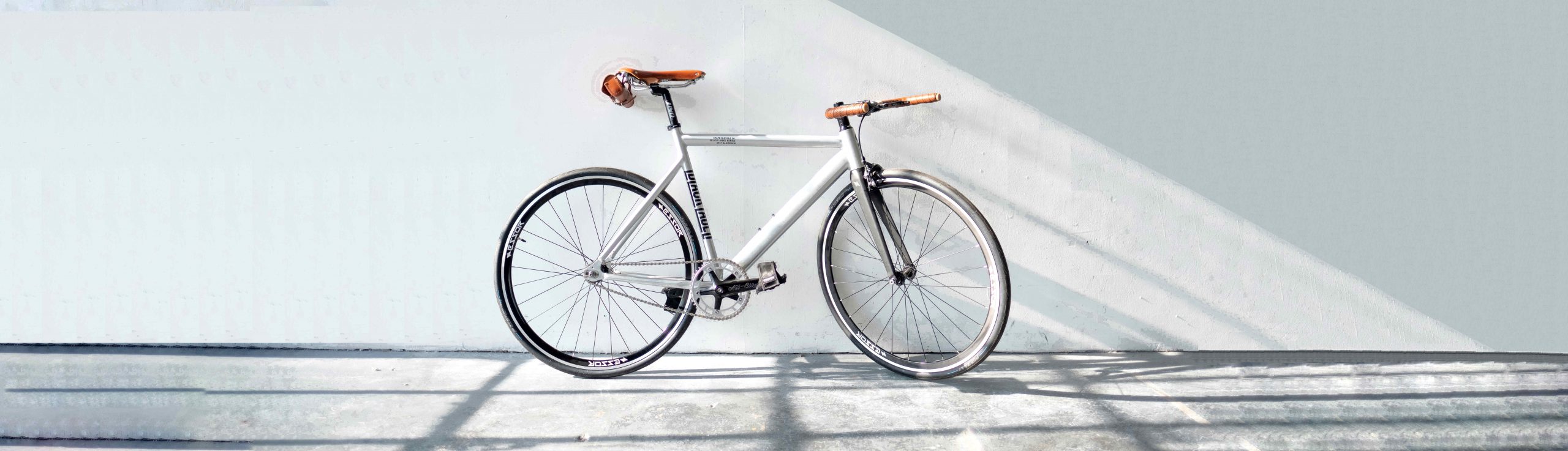 vélo blanc avec accessoires marron posé contre un mur blanc
